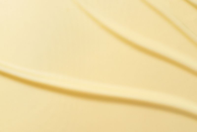 Abstract butter yellow color background. Lemon color silk satin fabric with soft wavy folds. Elegant background with space for text. Color of the year concept