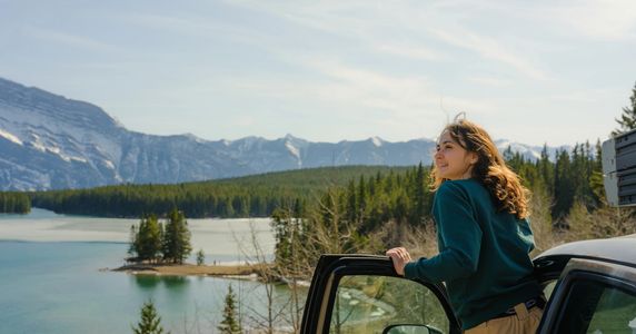 A woman enjoying a scenic mountain lake view from a car door.