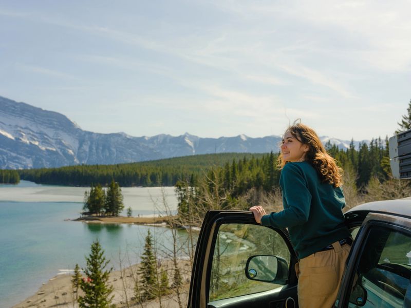 Woman looking at scenic lake along the road  in Banff during road trip with SUV in springtime