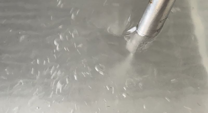 Water is sprayed forcefully from a metal nozzle creating a mist that forms fine droplets in the air.