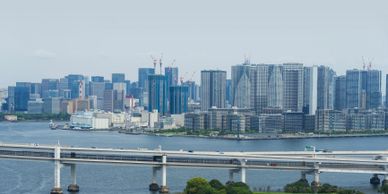 Modern city skyline with high-rise buildings by the water and a bridge in the foreground.