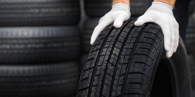 Person wearing white gloves holding a tire with a stack of tires in the background.