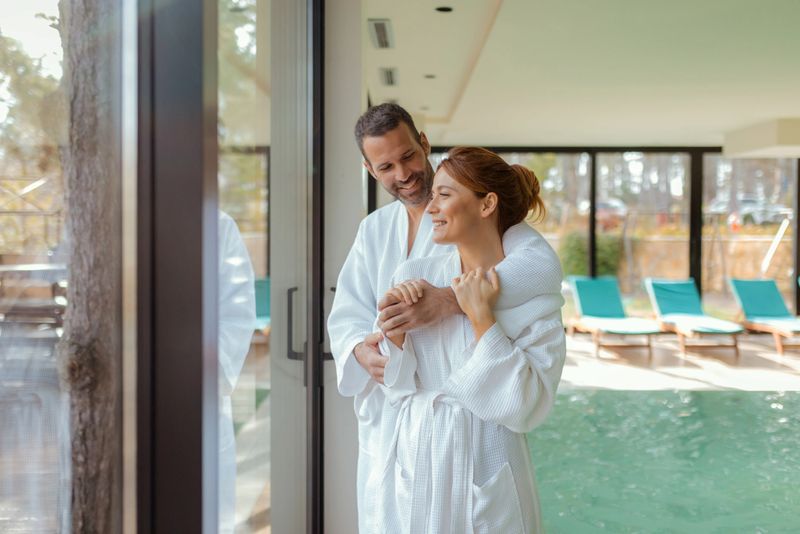 A Couple Stands Together in a Modern Spa Center, Embracing as They Take in the Beauty of Nature Through a Large Glass Window. A Representation of Love, Relaxation, and Wellness.