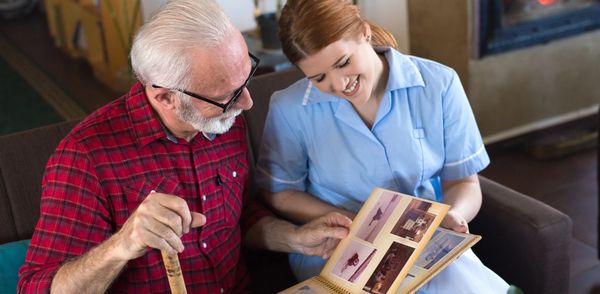 Nurse smiling warmly at elderly man on a couch.