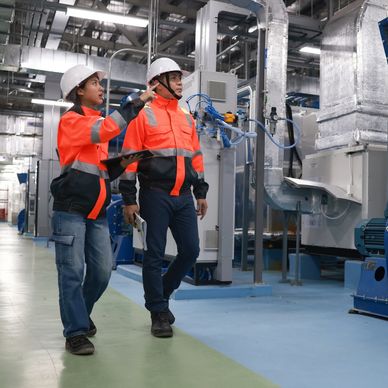 Two engineers in safety gear inspecting machinery inside a factory.