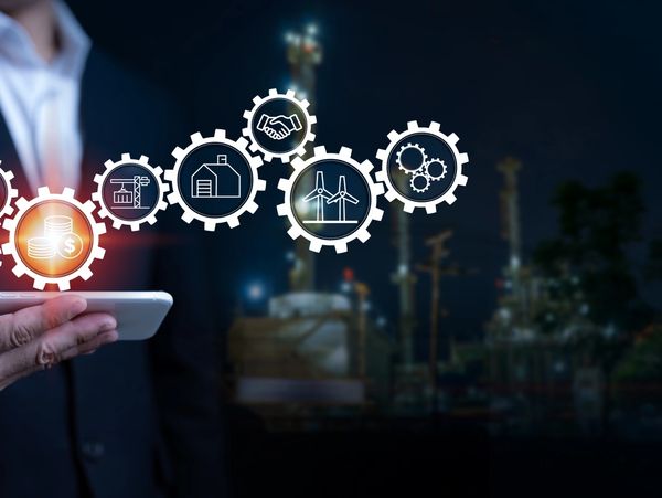 Businessman holding smartphone with industrial and financial icons floating above.