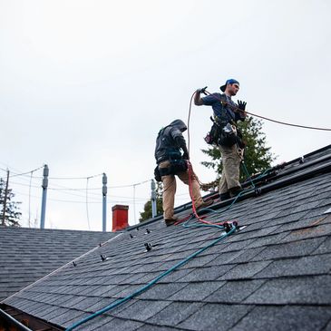 Two workers in safety gear install equipment on a sloped roof.