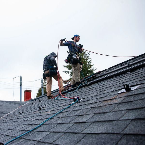 Two workers are securing ropes on a steep rooftop for safety.