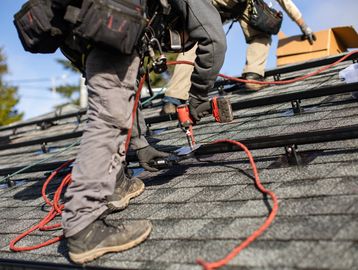 Two workers installing shingles on a roof.