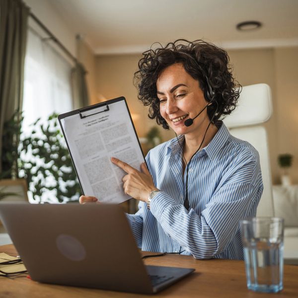 Woman with headset pointing to document during video call.