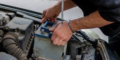 Person replacing a car battery under the hood.