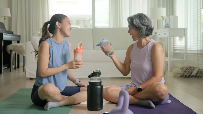 Young adult child active mature middle age old mum drink whey protein shake bottle diet food after home workout. Love health care older aged mom asia elder people happy relax sport protect aging life.