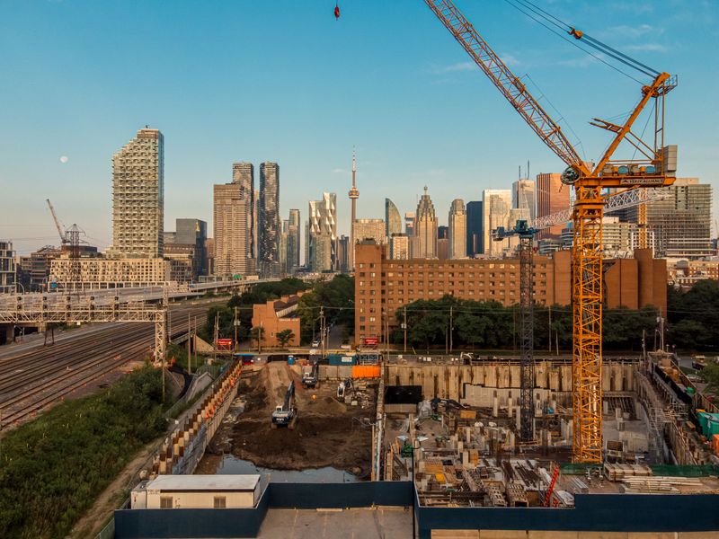 A construction site with cranes in front of the Toronto skyline during sunset, showcasing urban development and architecture.