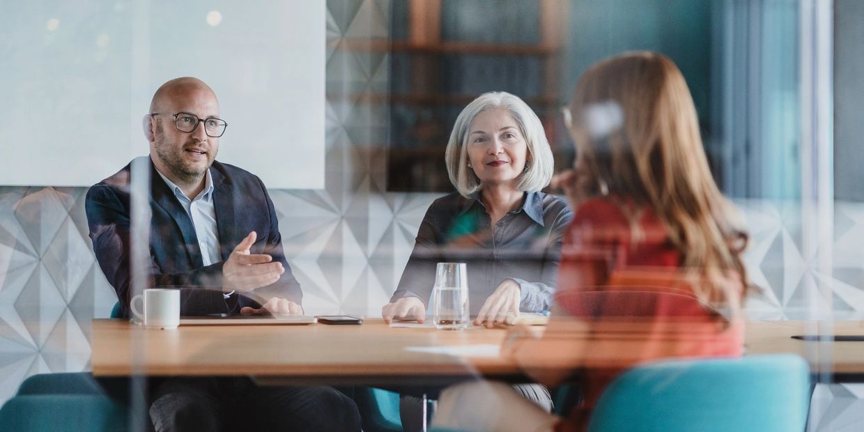 Two interviewers speaking with a candidate in a modern office.