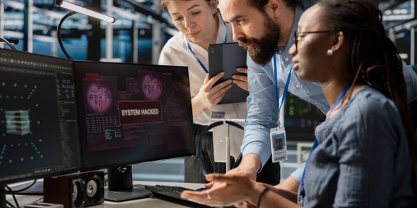 Team of cybersecurity experts addressing a system hack alert on computer screens.