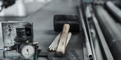 A hammer rests on a workbench surrounded by metal pipes and a pressure gauge.
