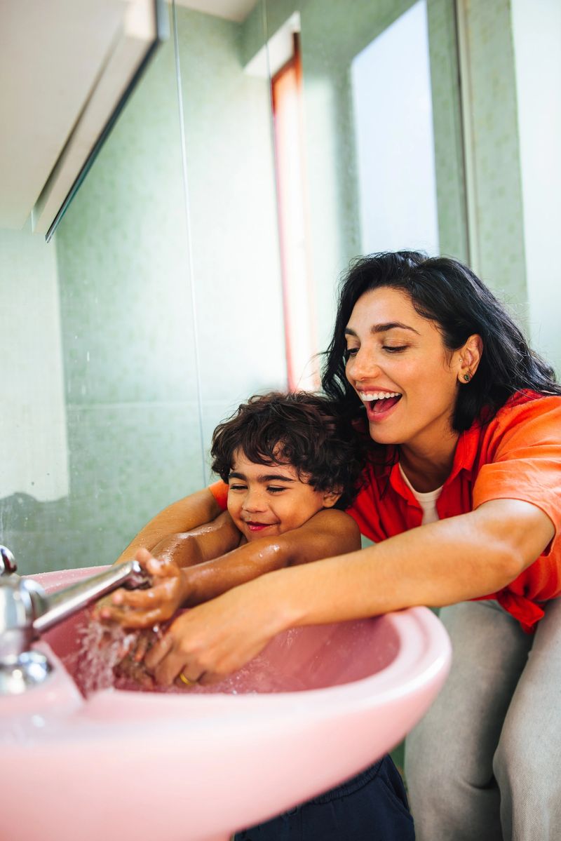 A Latina mother helps her young son wash his hands at the sink. Capturing family connection, joy, and teaching good hygiene habits, this moment highlights fostering responsibility in daily routines.