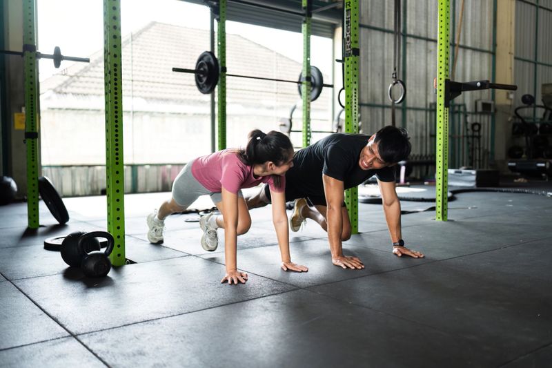 A man and woman engaging in a fun workout, doing mountain climbers, promoting teamwork and fitness.