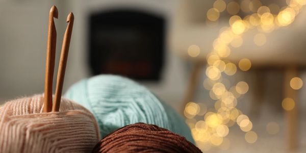 Cozy yarn balls with wooden crochet hooks and warm bokeh lights in the background.