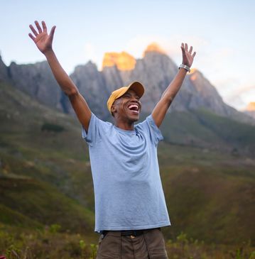 A joyful man with arms raised in front of mountains during sunset.