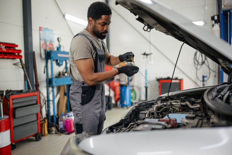 The mechanic checks the oil level in the engine bay, emphasizing the importance of oil maintenance in vehicle health within a bustling automotive repair workshop.