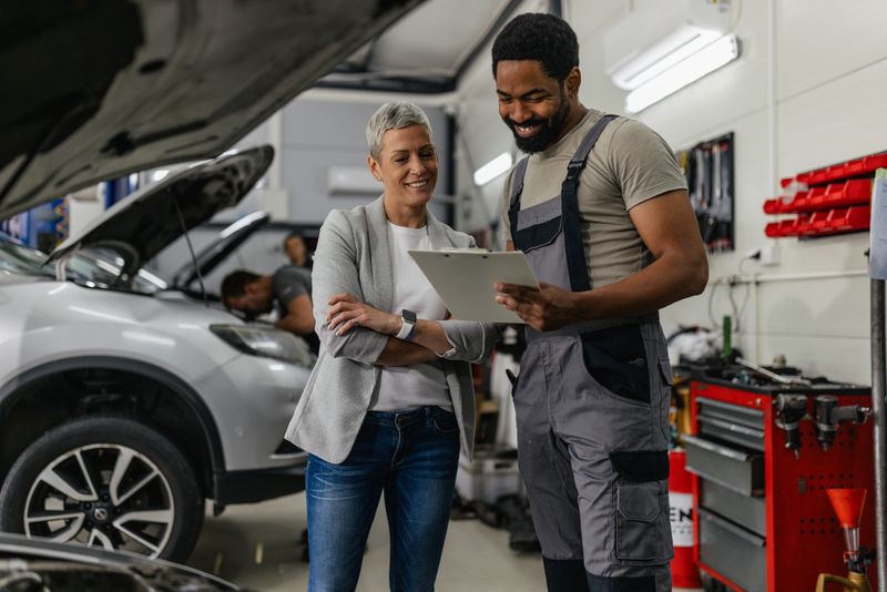 A mechanic converses with a client while reviewing a clipboard, highlighting effective communication and customer relations in the automotive service industry.