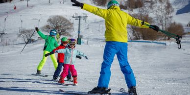 Ski instructor teaching three kids to ski on a snowy slope.