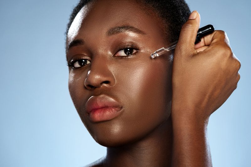 A woman gently applies a skincare serum to her cheek with a tool, showcasing a smooth complexion against a light blue background. The setting is bright and fresh, highlighting her focus.