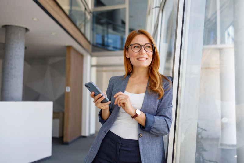 Smiling businesswoman engaging with her smartphone while working in a sleek, modern office building, radiating confidence and professionalism