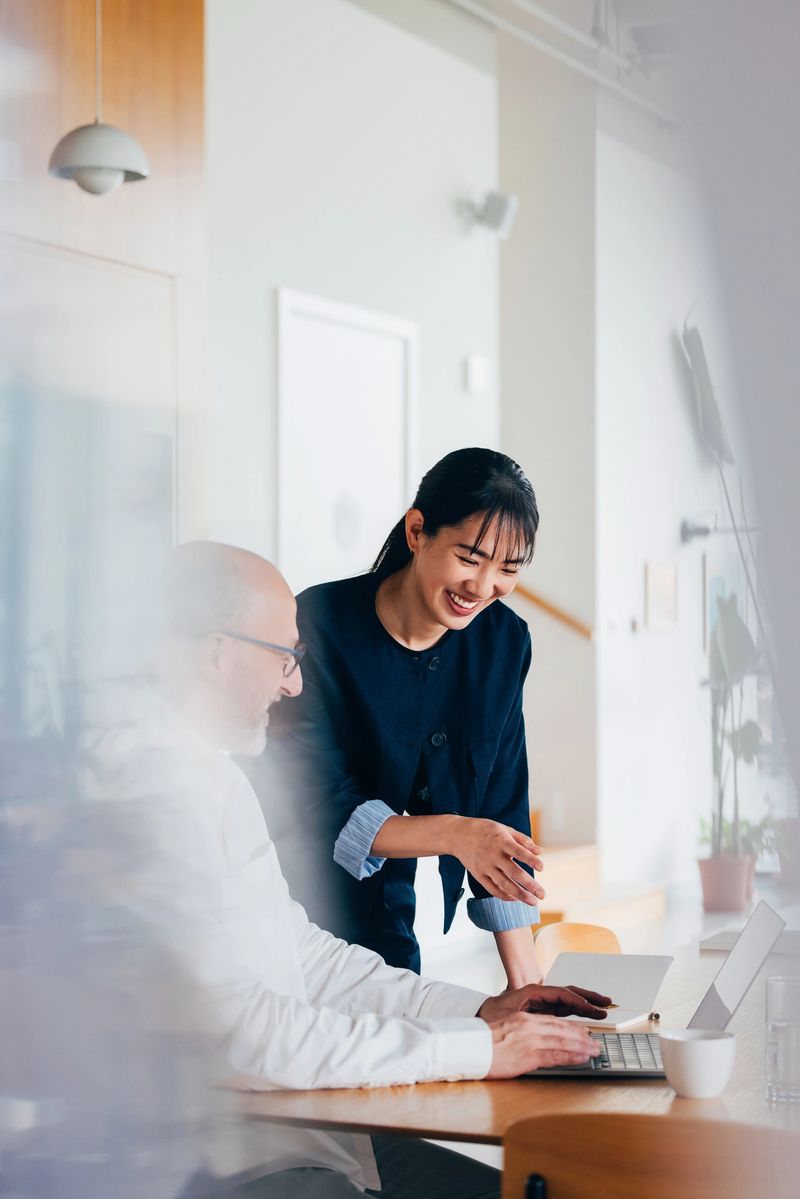 Two professional colleagues engaged in a collaborative discussion, surrounded by a contemporary office environment, fostering teamwork, communication, and productivity.