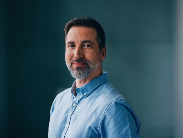 Confident middle-aged man with a beard wearing a blue shirt, smiling gently.