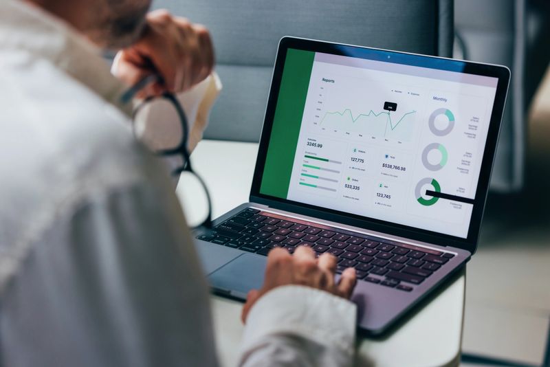 A professional focuses on analyzing detailed business reports displayed on a laptop screen. The graphics include various charts and performance metrics, highlighting statistical trends for comprehensive decision-making in a corporate environment.