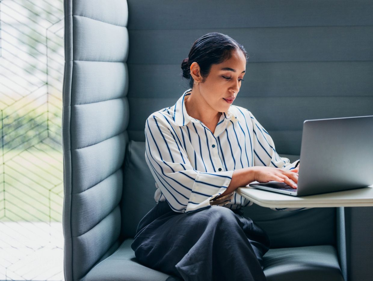 Woman working focused on laptop in a cozy office booth.