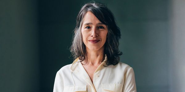 Confident middle-aged woman in a light blouse with arms crossed, smiling gently.