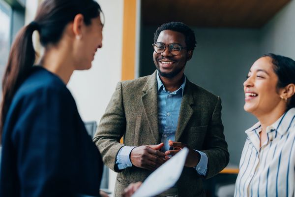 Three colleagues smiling and conversing in a bright office setting.