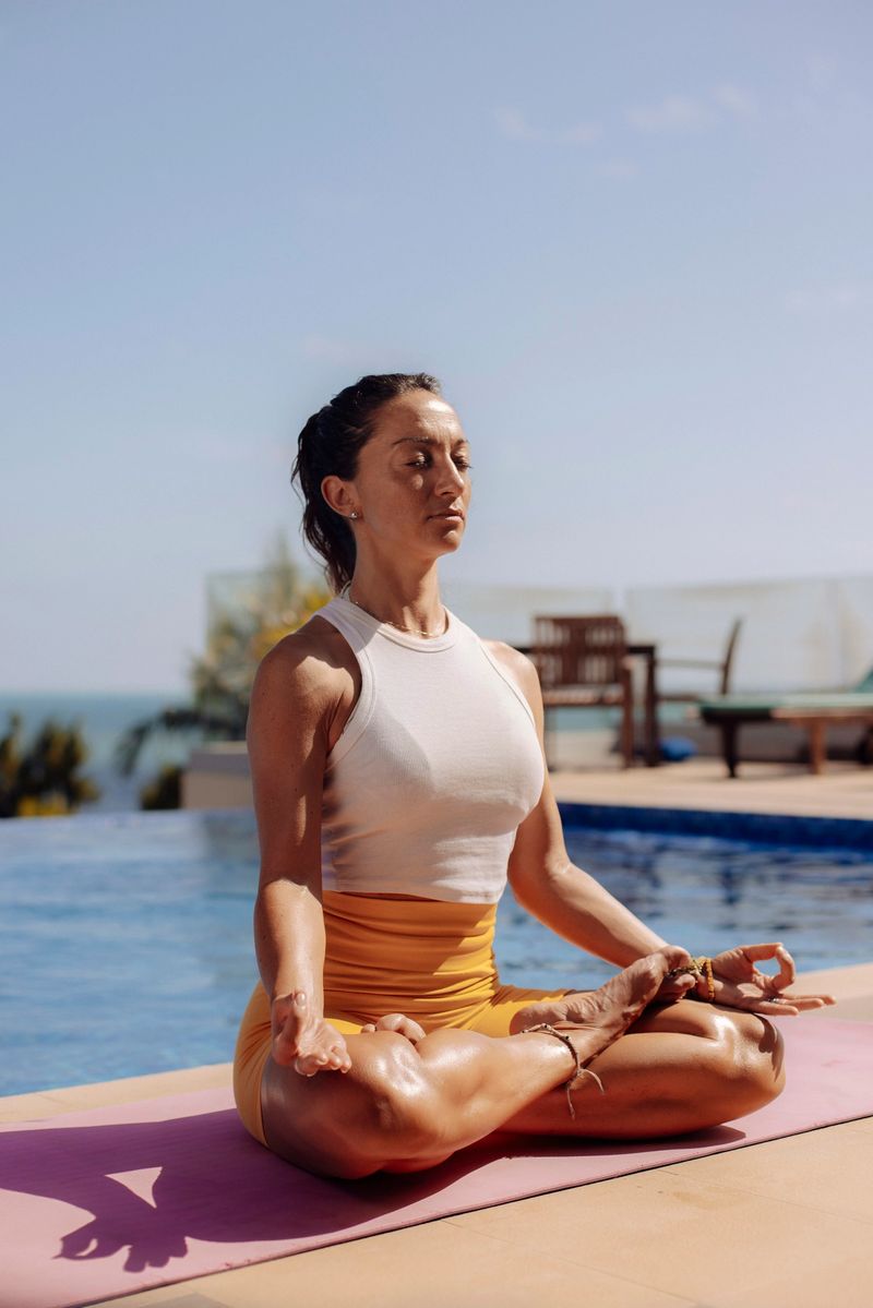 A serene moment of a focused woman meditating in a yoga lotus pose near a calm pool with ocean views