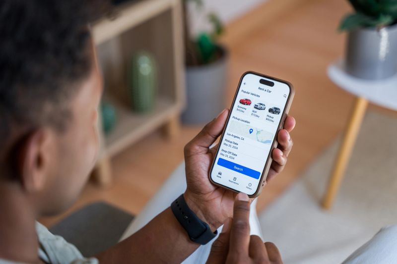 Close-up view of a young adult using a smartphone app for renting a vehicle while planning a trip in vibrant Los Angeles