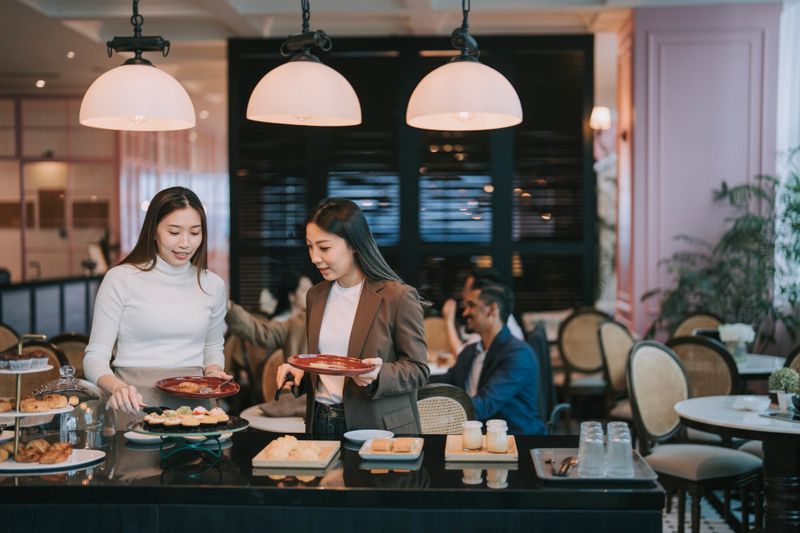 2 Asian businesswoman picking up food at buffet area in business conference meeting coffee break