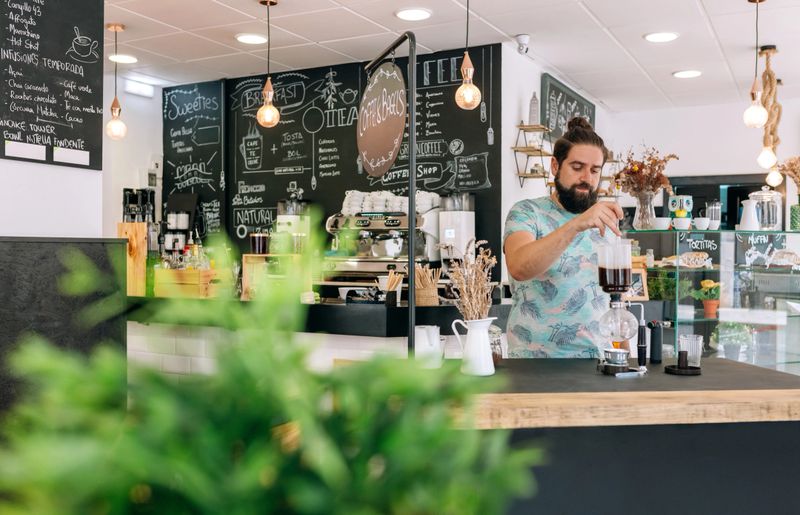 Barista skillfully prepares a specialty coffee with Japanese siphon coffee maker in modern cafe setting stylish decor and cozy atmosphere, surrounded by chalkboard menus.