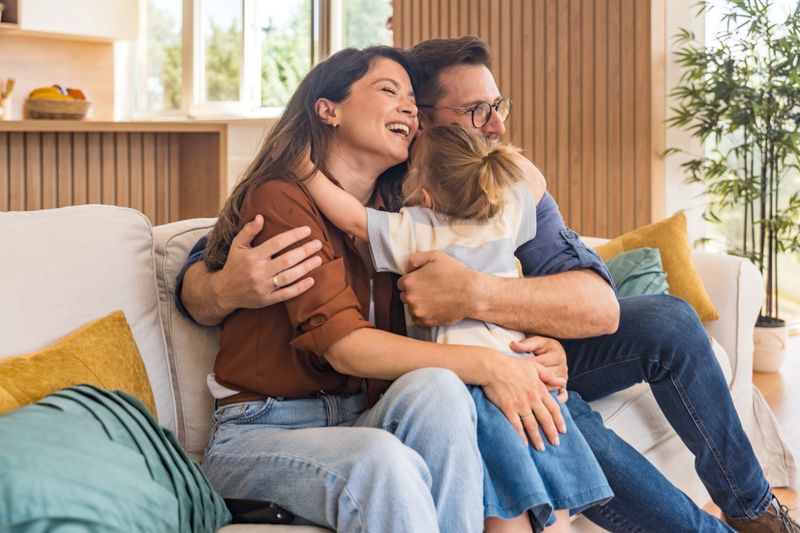 Happy young family with child enjoying new home after moving in  unpacking boxes, relaxing in living room, spending time together in kitchen, celebrating new beginning. Man, woman and daughter.
