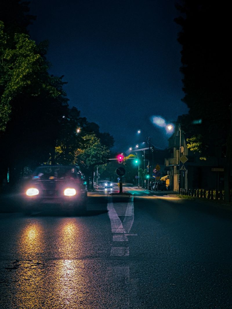 Urban street scene at night with glowing headlights of a passing car, reflecting lights, and atmospheric city environment. Taken in a small town in Europe.