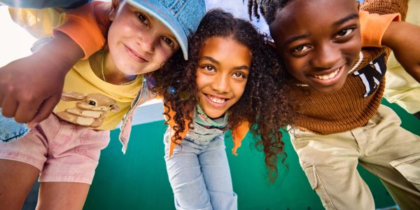 Three kids smiling and leaning toward the camera.