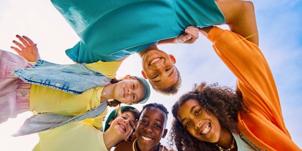 A group of five diverse friends smiling together under a blue sky.