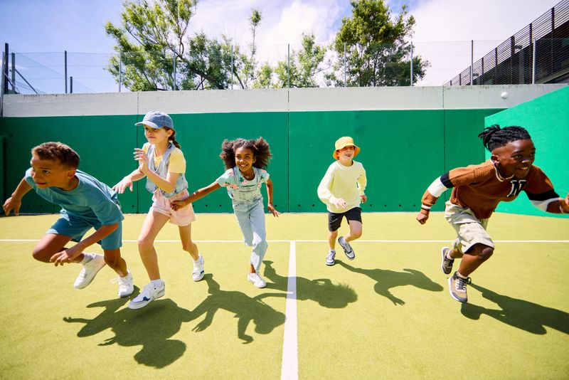 Diverse group of schoolchildren running across a vibrant green sports field, enjoying a sunny day of playful activity and promoting diversity