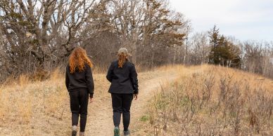 Two people walking on a trail in a dry, wooded area.