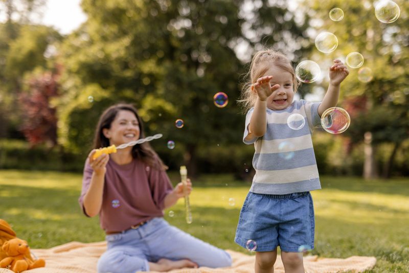 A joyful child laughing while playing with bubbles in a sunlit park.
