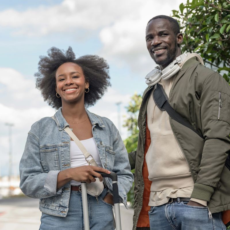 African American tourist couple on a city break, crossing the street holding hands and pulling their wheel suitcases. Travel adventure concepts.