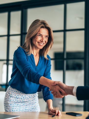 Smiling woman in blue blouse shaking hands in an office setting.
