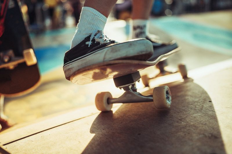 Close-up view of a surfskate skateboarder preparing to drop into a ramp at skate park. The skateboarder’s shoes and deck with visible wear emphasize the passion and dedication of the skating community. The vibrant background and summer atmosphere add energy to the scene.