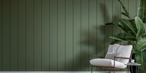 Cozy chair with plant against green paneled wall.